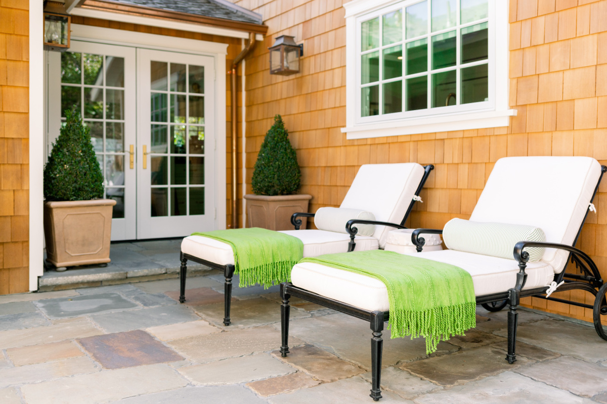 Chaise lounges on patio with green throw and boxwoods