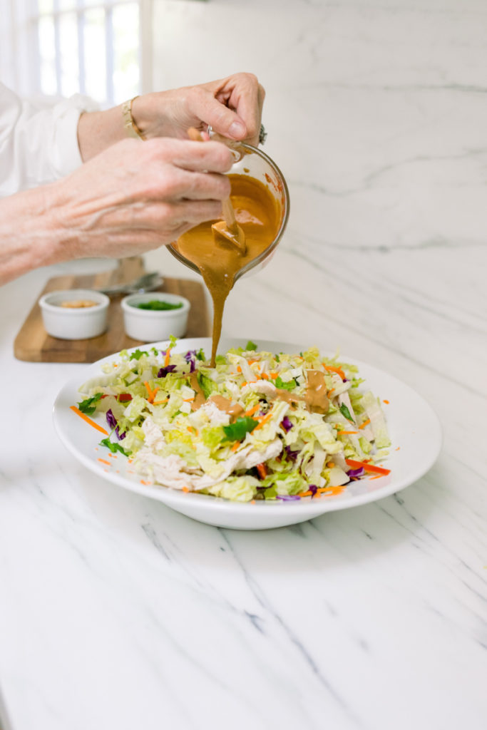 Adding dressing to bowl of Asian chicken salad