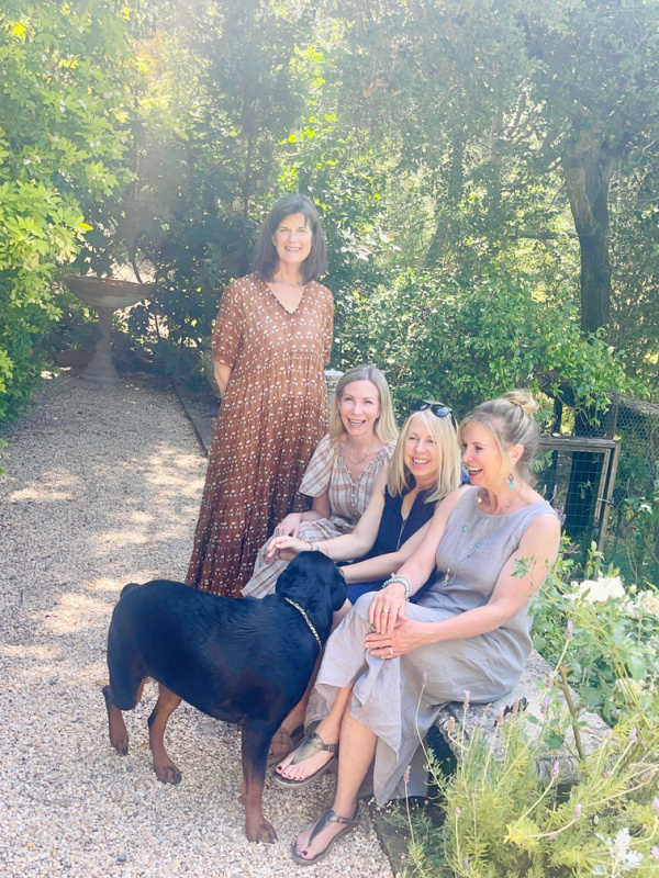 Four woman sitting on garden bench with dog