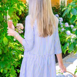 Woman holding cocktail and flower basket in garden Rose Hibiscus Spritz