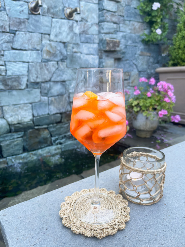 Aperol Spritz cocktail and candle on outdoor ledge.