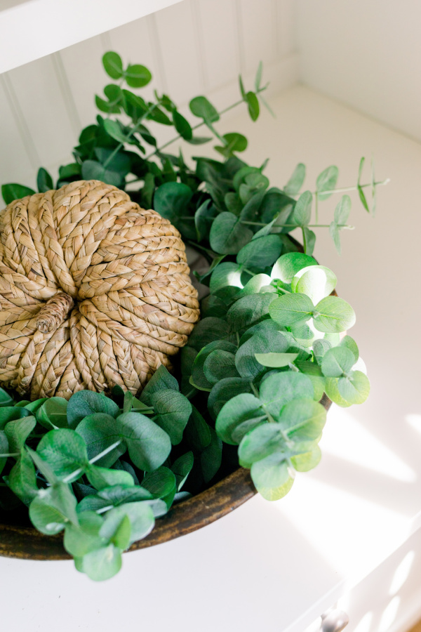 Woven pumpkin in a wooden bowl filled with eucalyptus.