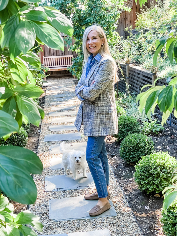 Woman in plaid jacket and striped shirt standing in garden. 