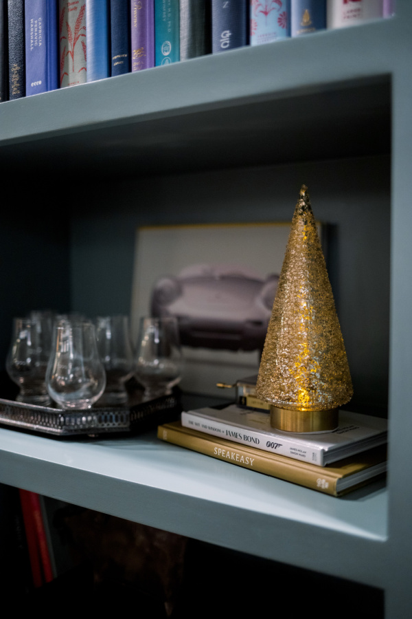 Gold glitter tree on top of books next to tray of bourbon glasses.