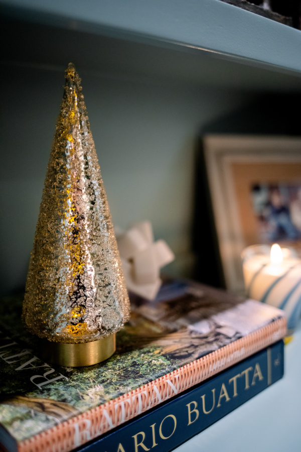 Gold glitter Christmas tree sitting on top of books on a shelf.
