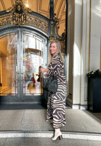 Woman entering Palace Hotel wearing animal print shirtdress.