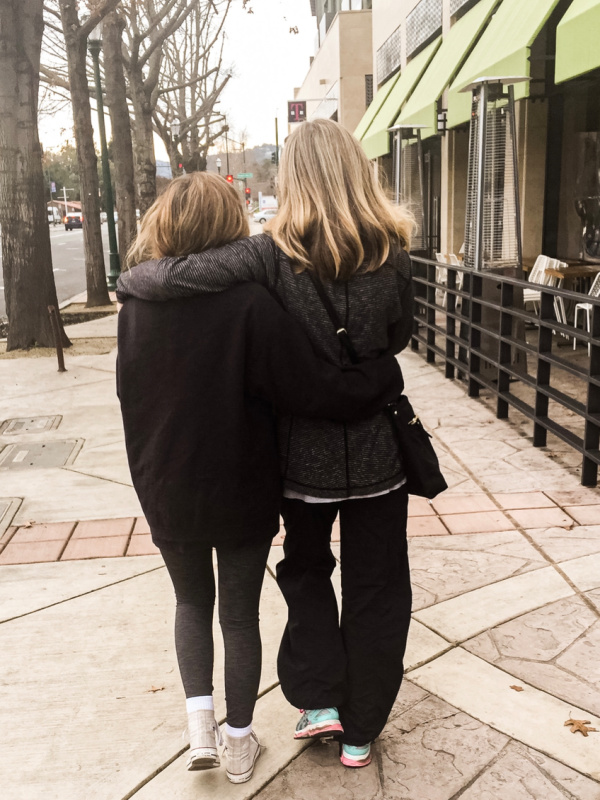Two woman walking down street with arms around each other.