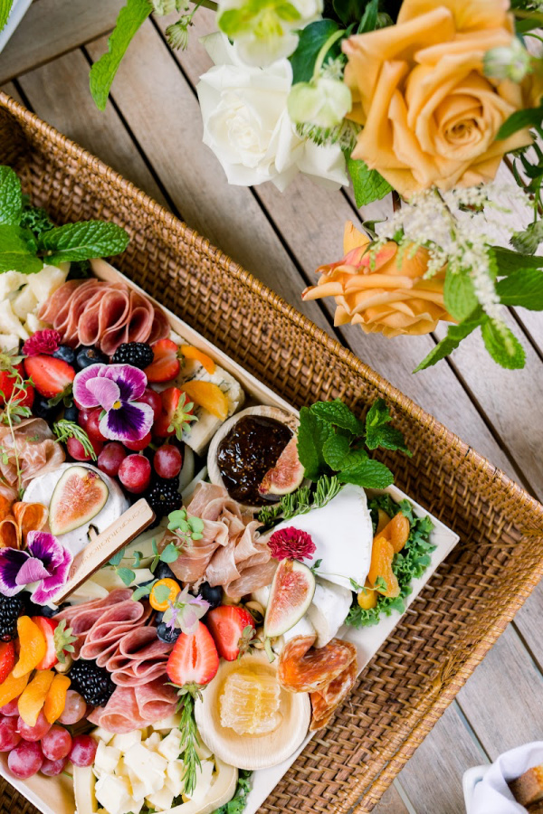 Charcuterie tray in basket next to floral arrangement.