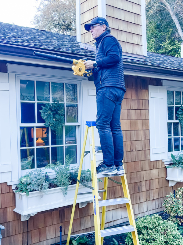 Man on ladder cleaning house gutters.