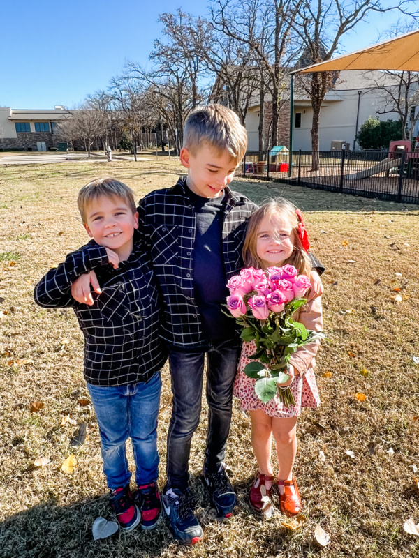 Three children in a playground, holding flowers.
