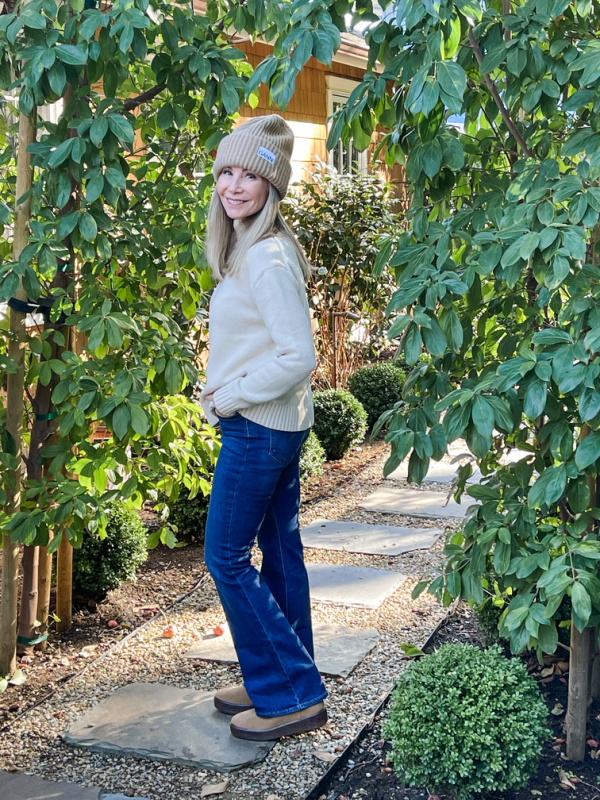 Woman win jean's sweater and beanie standing in garden.