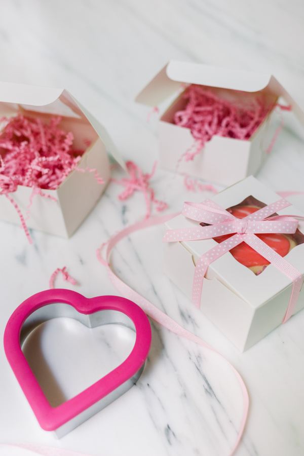 Heart shaped cookie cutter with white bakery boxes and pink confetti.