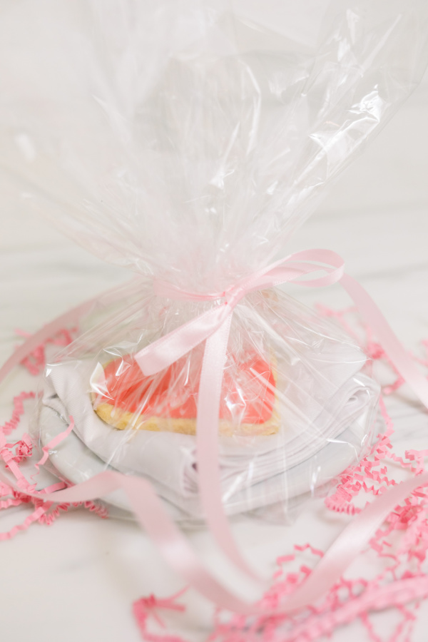 Heart shaped cookie on plate wrapped with cellophane and surrounded with pink confetti.