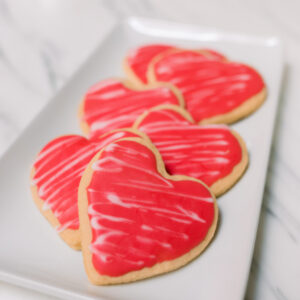 Pink frosted heart shaped cookies on white tray.