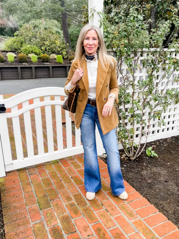Woman wearing corduroy blazer and denim standing in front of white fence.