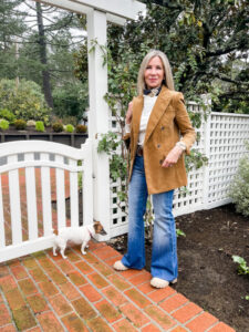 Woman wearing corduroy blazer and denim standing in front of white fence.