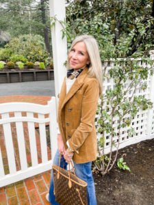 woman wearing corduroy blazer and jeans standing in front of white fence.