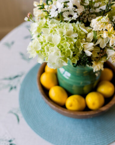 White floral bouquet in green pitcher surrounded by lemons.