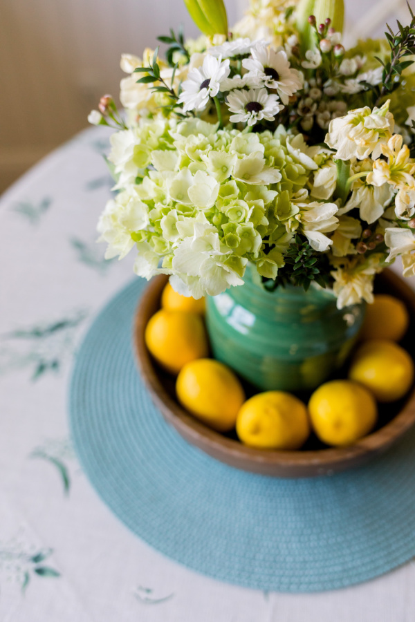 White floral bouquet in green pitcher surrounded by lemons.