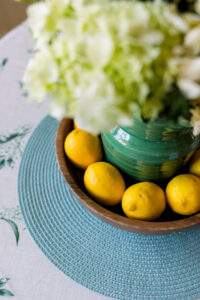 Flowers in green vase surrounded by lemons.
