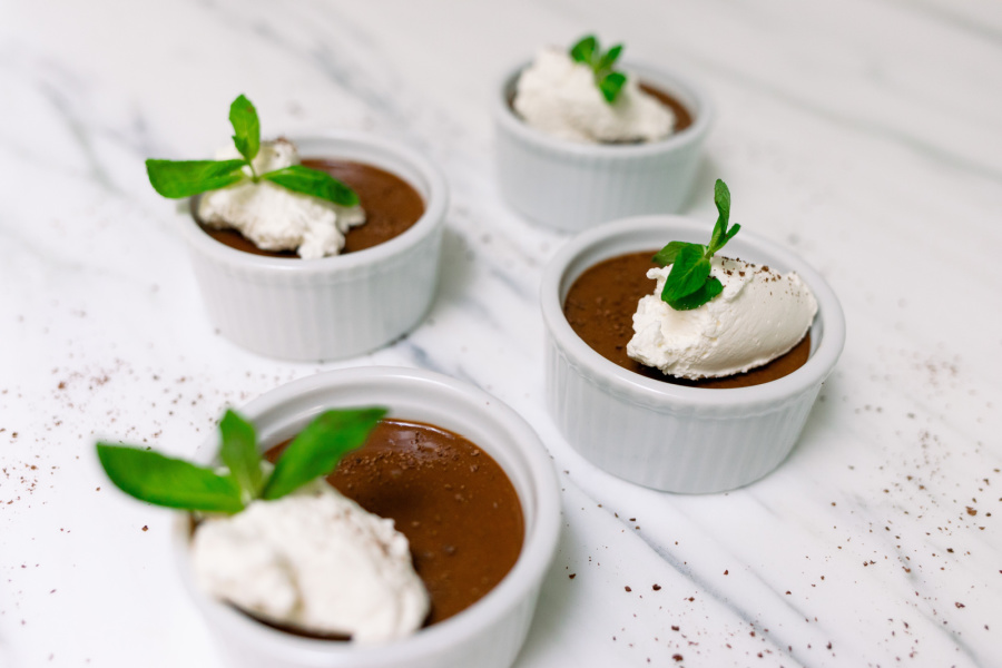 Ramekins filled with chocolate pots de creme with whip creme and mint sprigs on top.