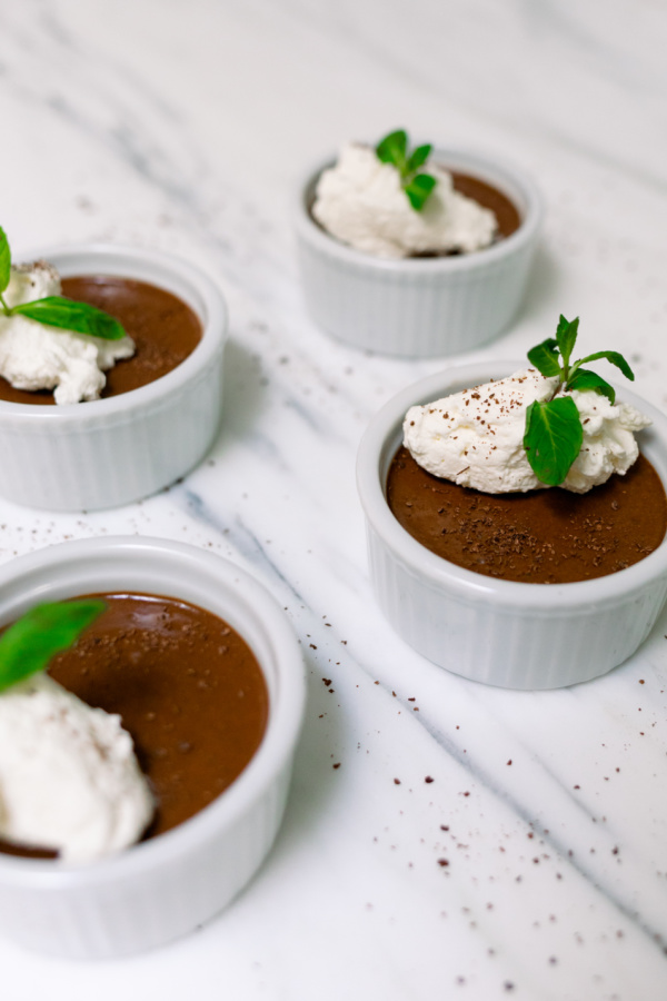 Four chocolate pots de creme topped with whipped cream and mint.