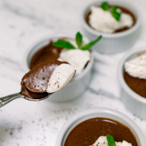 Ramekins filled with chocolate pots de creme with whip creme and mint sprigs on top.
