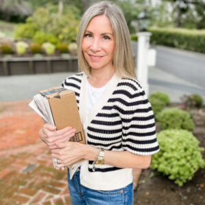 Woman wearing stripped cardigan holding package and newspaper.