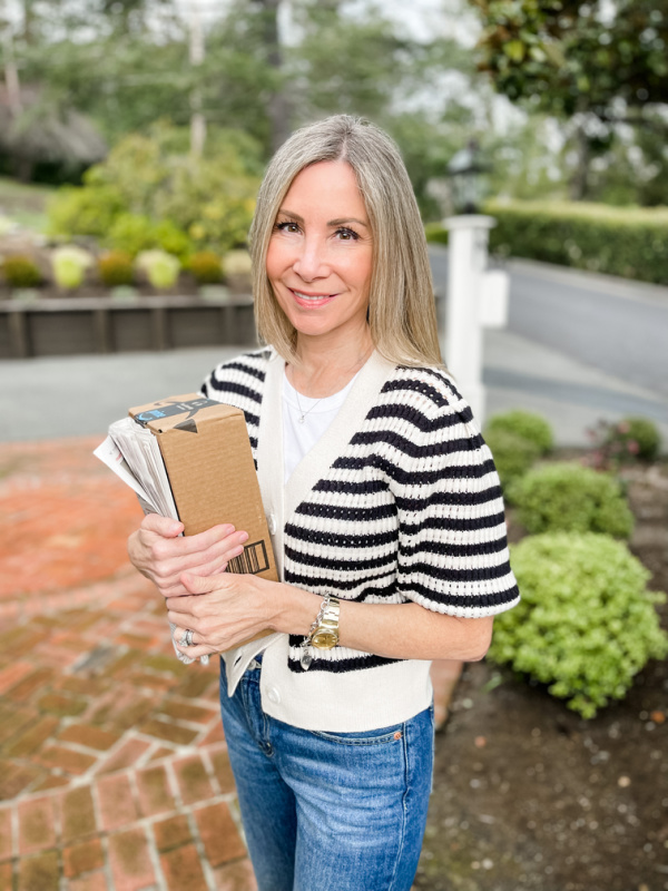 Woman wearing stripped cardigan holding package and newspaper.