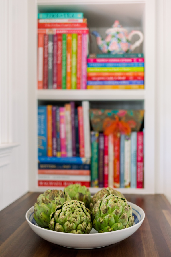 Cookbook shelves and a bowl of artichokes.
