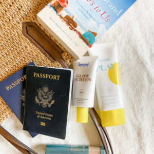 Passports, sunscreen and beach read on straw tote.
