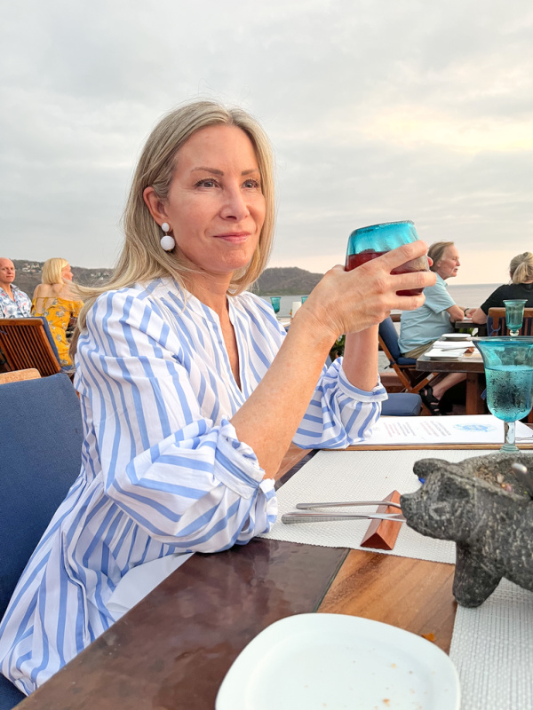 woman sitting at ocean front table with cocktail.