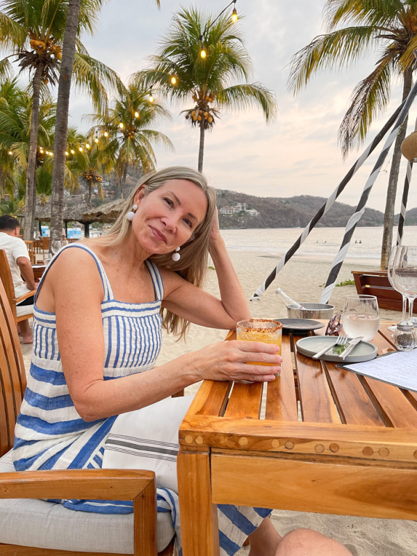 Woman at table on the beach with cocktail.