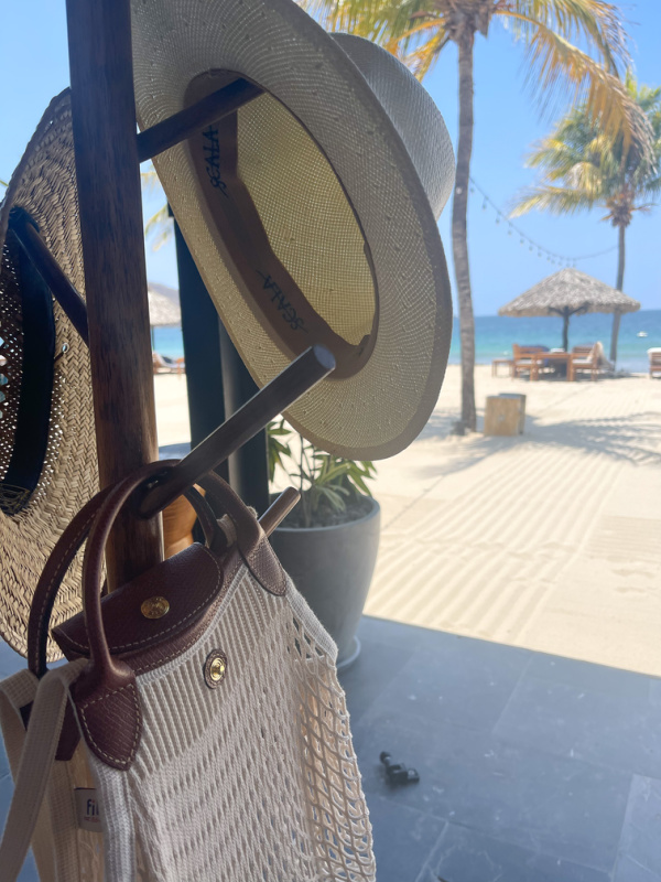 Two hats and a beach bag on hat rack on beach.