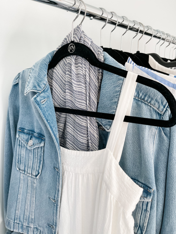 Denim jacket and white dress with scarf on rack.