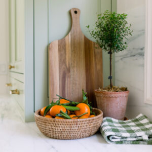 Kitchen vignette with cutting board leaning against counter, topiary and bowl of oranges.