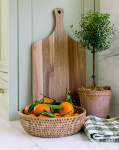 Kitchen vignette with cutting board leaning against counter, topiary and bowl of oranges.