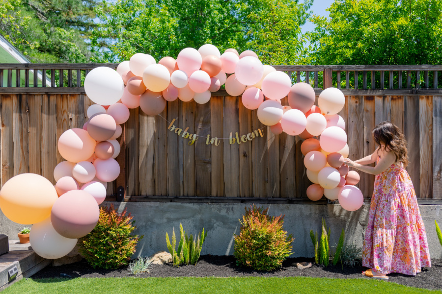 Woman in pretty floral dress setting up baby girl shower balloon arch.
