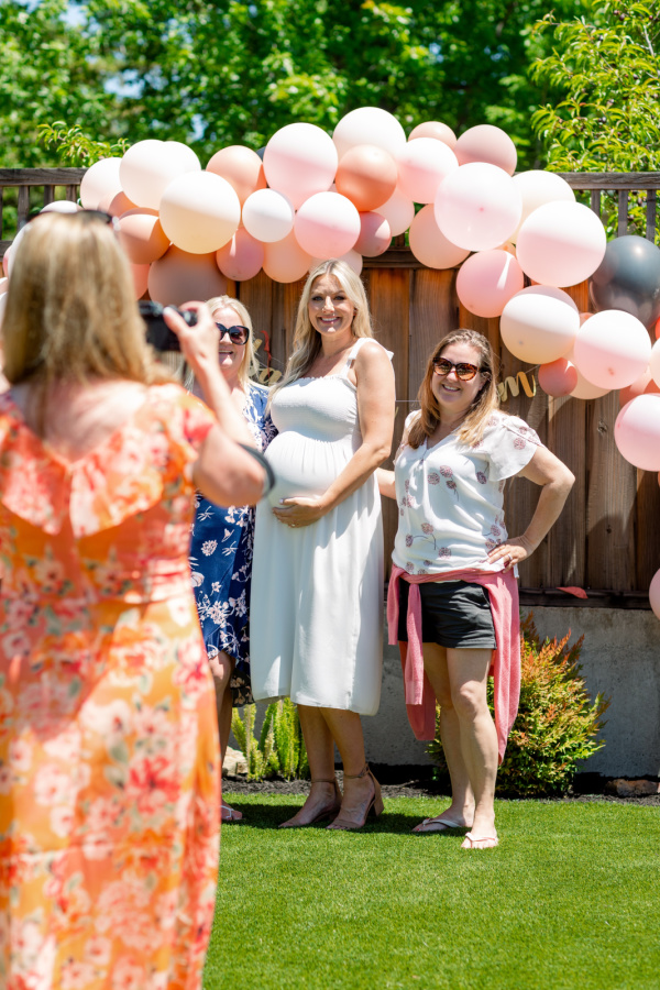 Woman taking pictures of pregnant woman and guests at baby shower.
