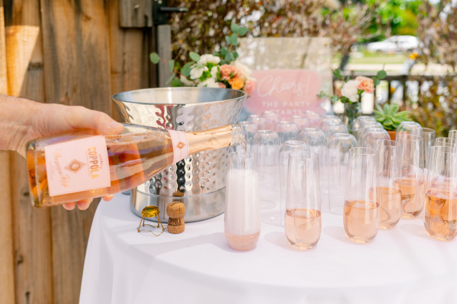 Baby shower welcome drinks table, pouring rose Prosecco into glasses.