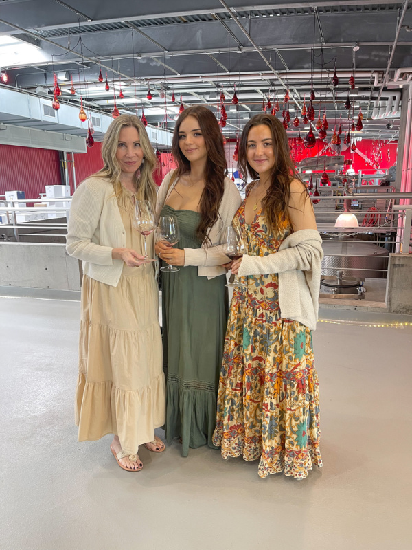Three woman standing in a winery cellar holding wine glasses.