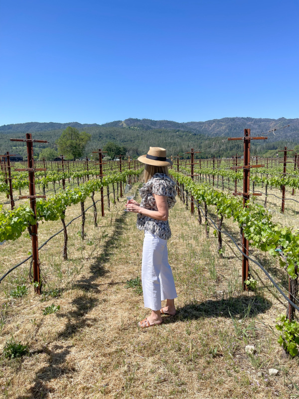 Woman wearing white pants and hat standing in a Napa Valley vineyard.