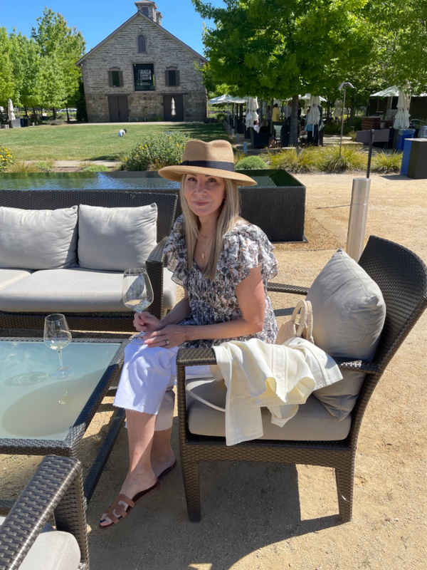 Woman wearing hat sitting and sipping wine in Hall Wendy gardens.