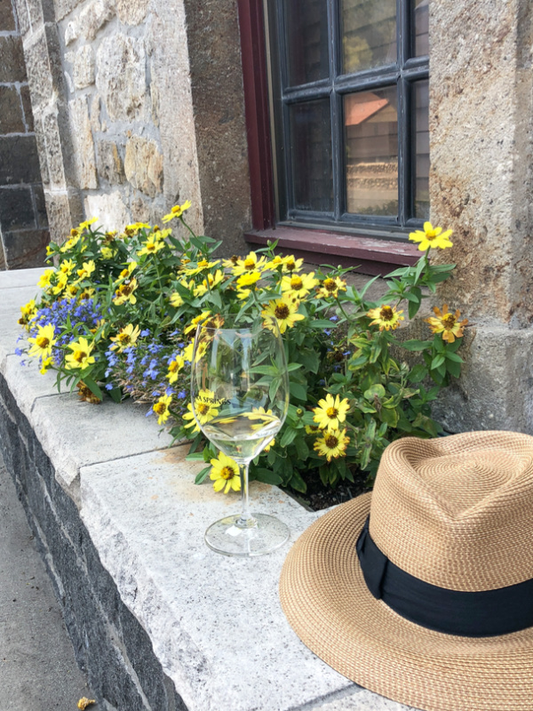 Stone ledge with glass of white wine sitting on top alongside straw hat.