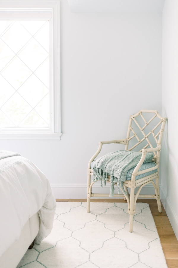 White rattan chair with blue throw blanket in corner of bedroom.