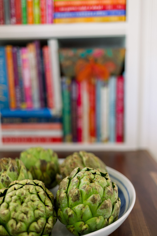 Bowl of artichokes on counter with cookbook shelves in background.