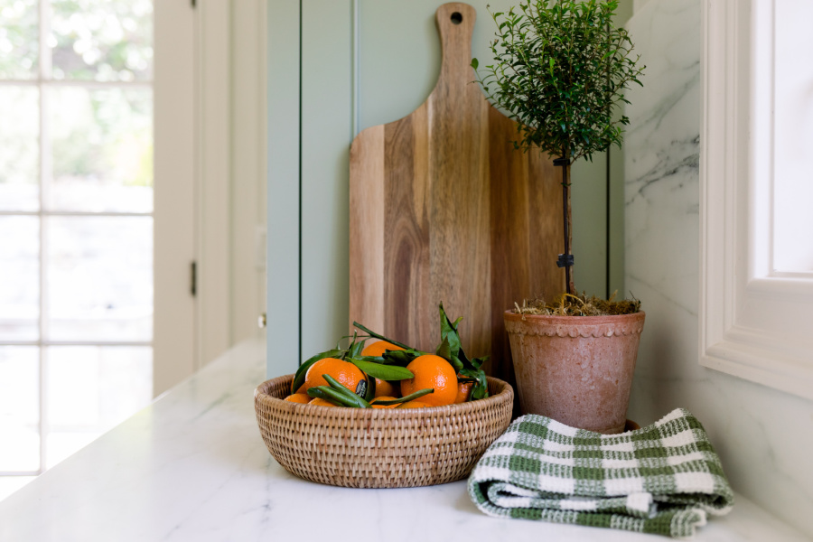 woven bowl filled with tangerines on green kitchen cabinets.