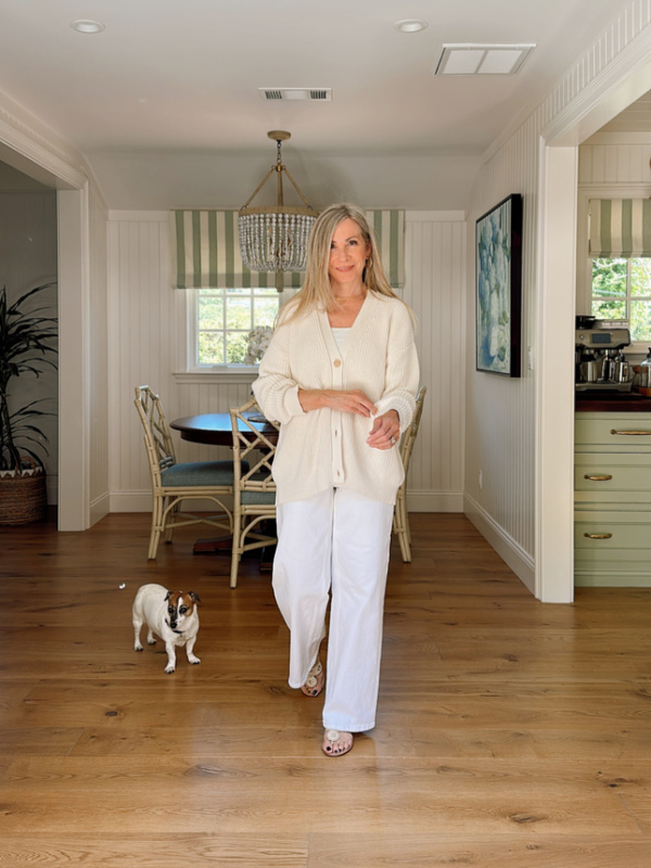 Woman wearing white jeans, ivory cardigan standing next to Jack Russell Terrier.