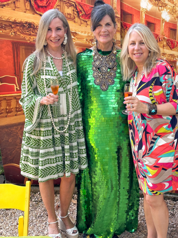 Three woman standing in front of opera house backdrop at garden party.