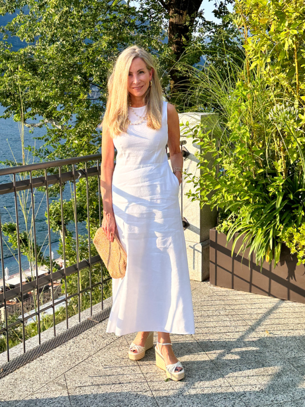 Woman standing on balcony overlooking Lake Como wearing white linen dress.